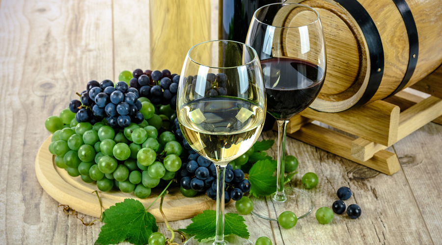 Foto di due calici di vino, uno bianco e uno rosso,  con accanto un tagliere ricoperto di uva. 