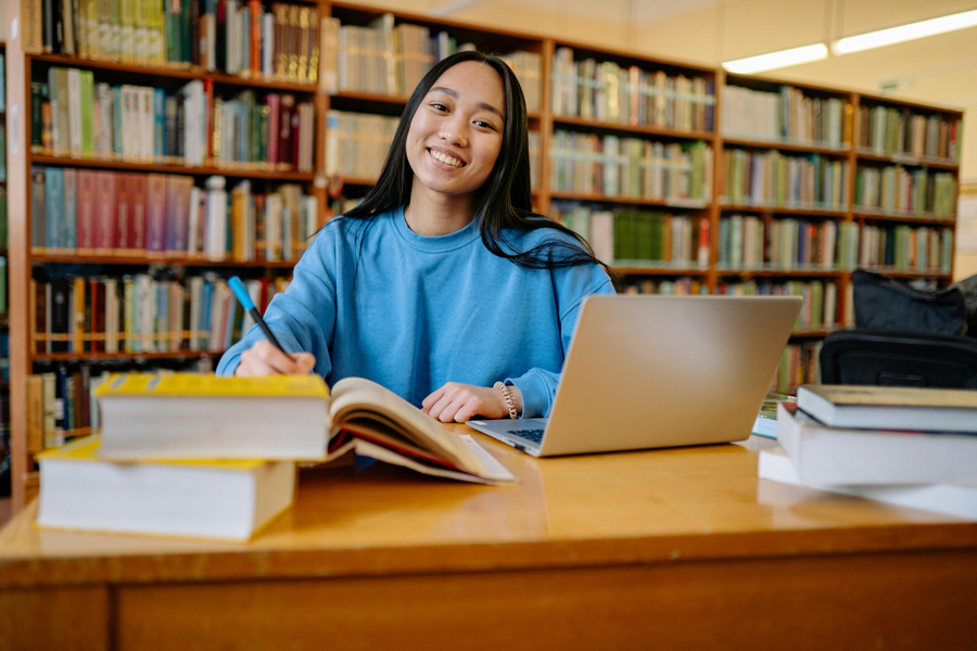 Ragazza in biblioteca con libri quaderni e appunti di scrittura