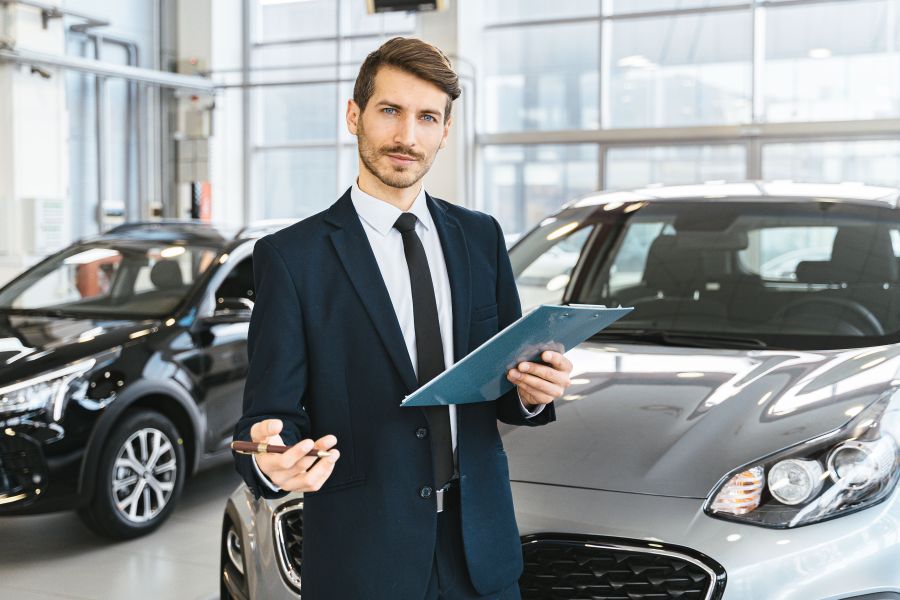 Concessionario d'auto professionale in abito che tiene un cartellino in un luminoso showroom di auto