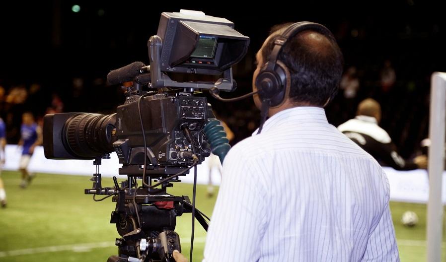 uomo di spalle che riprende una partita di calcio con una videocamera