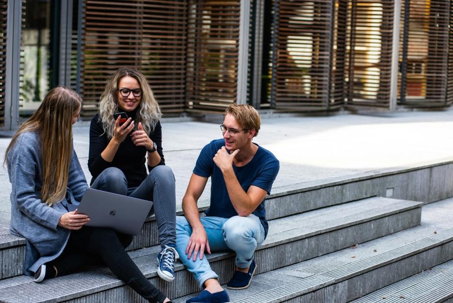 Immagine di tre ragazzi sulle scalinate dell'università con cellulare in mano e computer