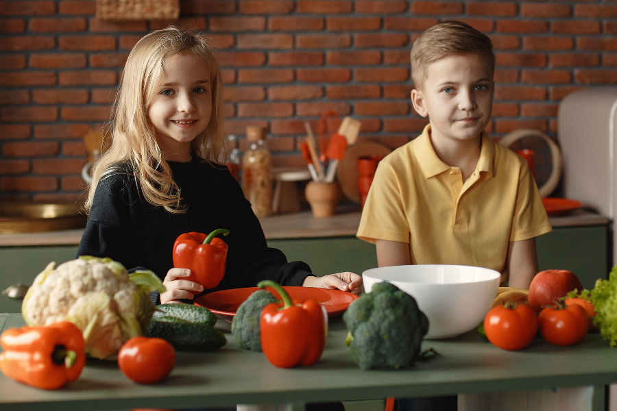 Due bambini che sorridono davanti a della verdura colorata