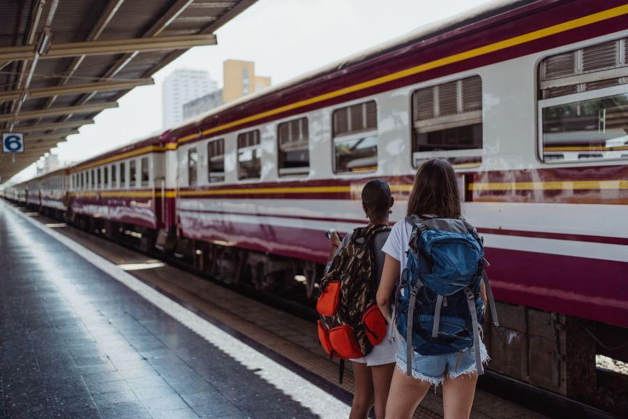 Due donne con zaini aspettano su una piattaforma ferroviaria, pronte per un'avventura.