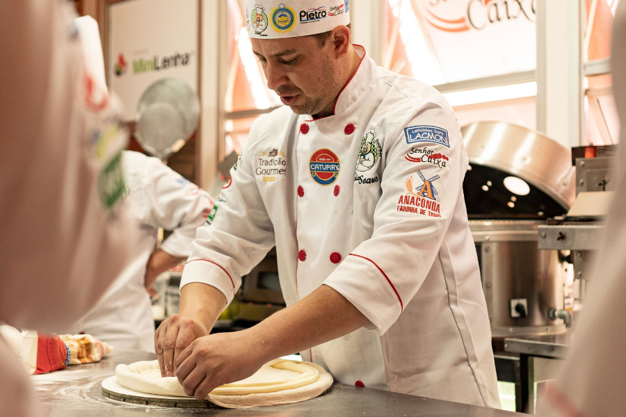 Chef che lavora l'impasto in una cucina professionale, mostrando abilità culinarie e dettagli dell'uniforme.