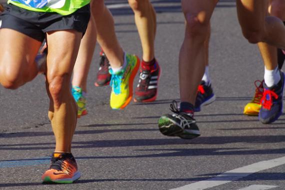 Foto di persone che corrono riprese dalle gambe in giù. Piedi che corrono su strada asfaltata.