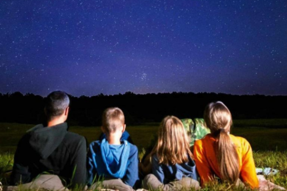Foto di quattro persone di spalle semi-sdraiate su un prato che guardano il cielo di notte.