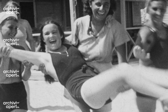 Foto in bianco e nero.Tre ragazze sorreggono una quarta ragazza tenendola per le braccia e le gambe. Tutte le ragazze ridono e si divertono