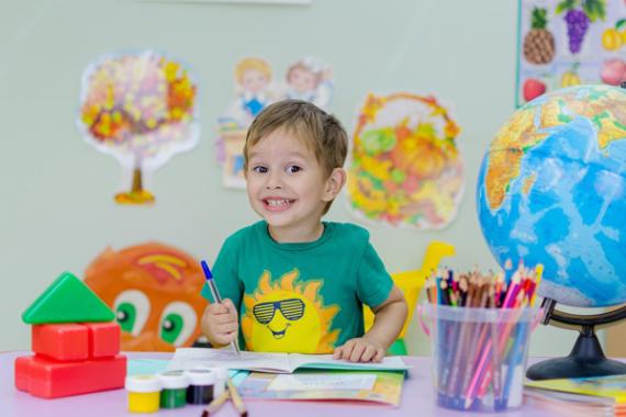 Foto di un bambino che scrive su un quaderno seduto a un tavolo. Sul tavolo ci sono colori, matite e un mappamondo.