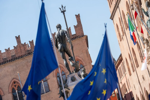 Immagine della città di Bologna, in particolare della statua del Nettuno e di uno dei palazzi di Piazza Maggiore con in primo piano bandiere dell'Europa.