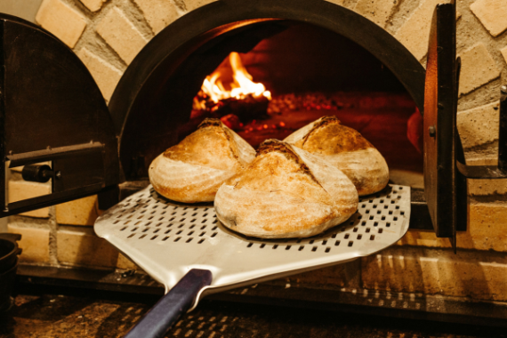 Tre pagnotte di pane a lievitazione naturale cuociono in un forno di mattoni rustico, mostrando l'artigianato culinario tradizionale.
